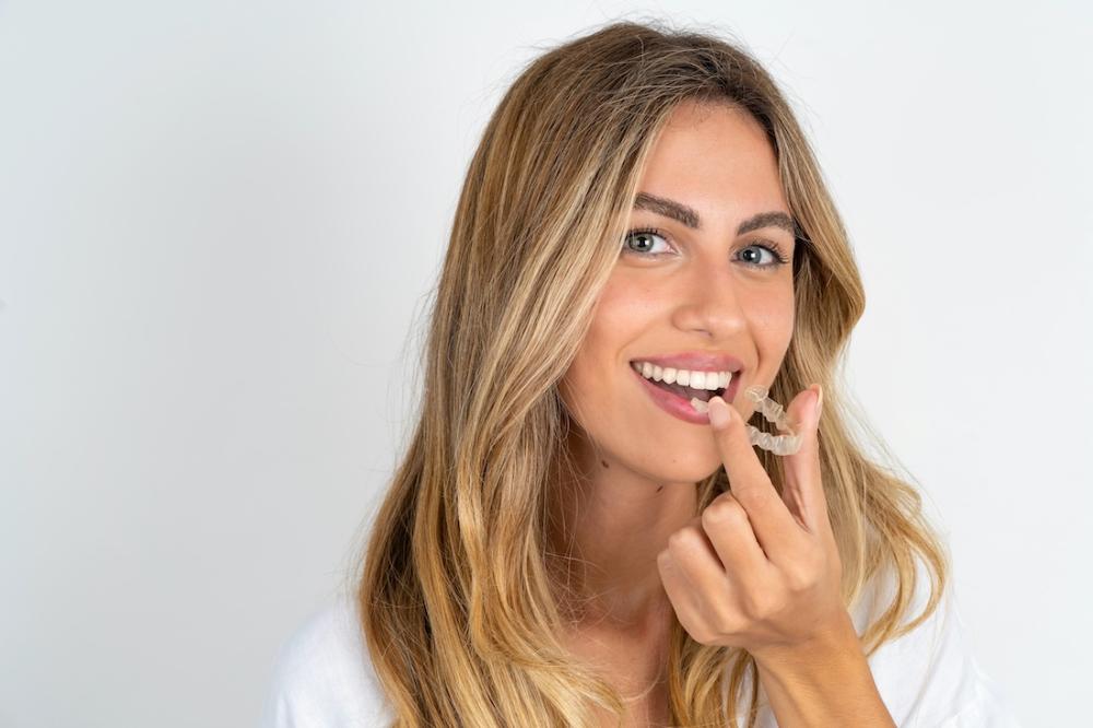 A smiling woman putting in an Invisalign tray