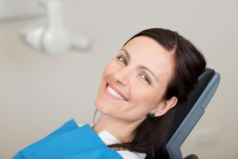 Smiling woman in dental chair after procedure
